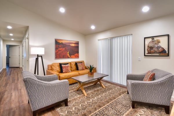 Open-plan living room and kitchen with tan leather sofa, patterned armchair, flat-screen TV, dark wood cabinetry, and dining table.