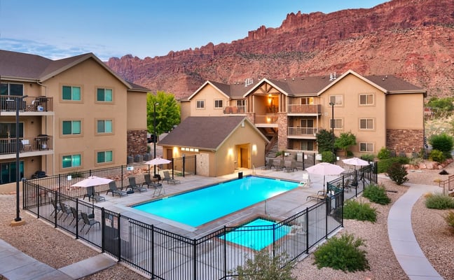 Resort-style apartment complex with swimming pool, hot tub, and red rock cliffs in background